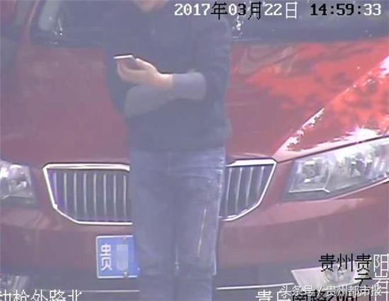 看到监控探头对着自己的车，男子站在车前用身体挡住车牌。