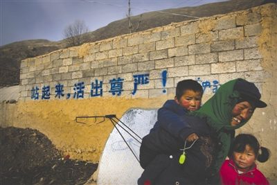 一位小寨村村民带着两名孩子从村口的宣传标语前走过 资料图片