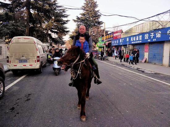 父子俩骑马走过街道本报记者李小刚摄