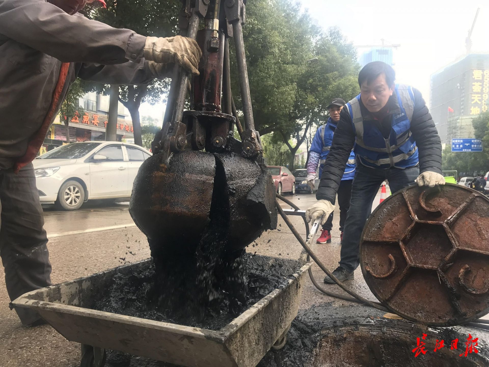 江汉区常青五路马路中央,刚刚研制完成的深井抓泥机正在进行打捞窨井
