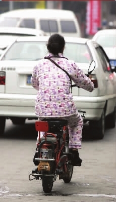 穿着睡衣,骑着电动车,穿行在车流中.